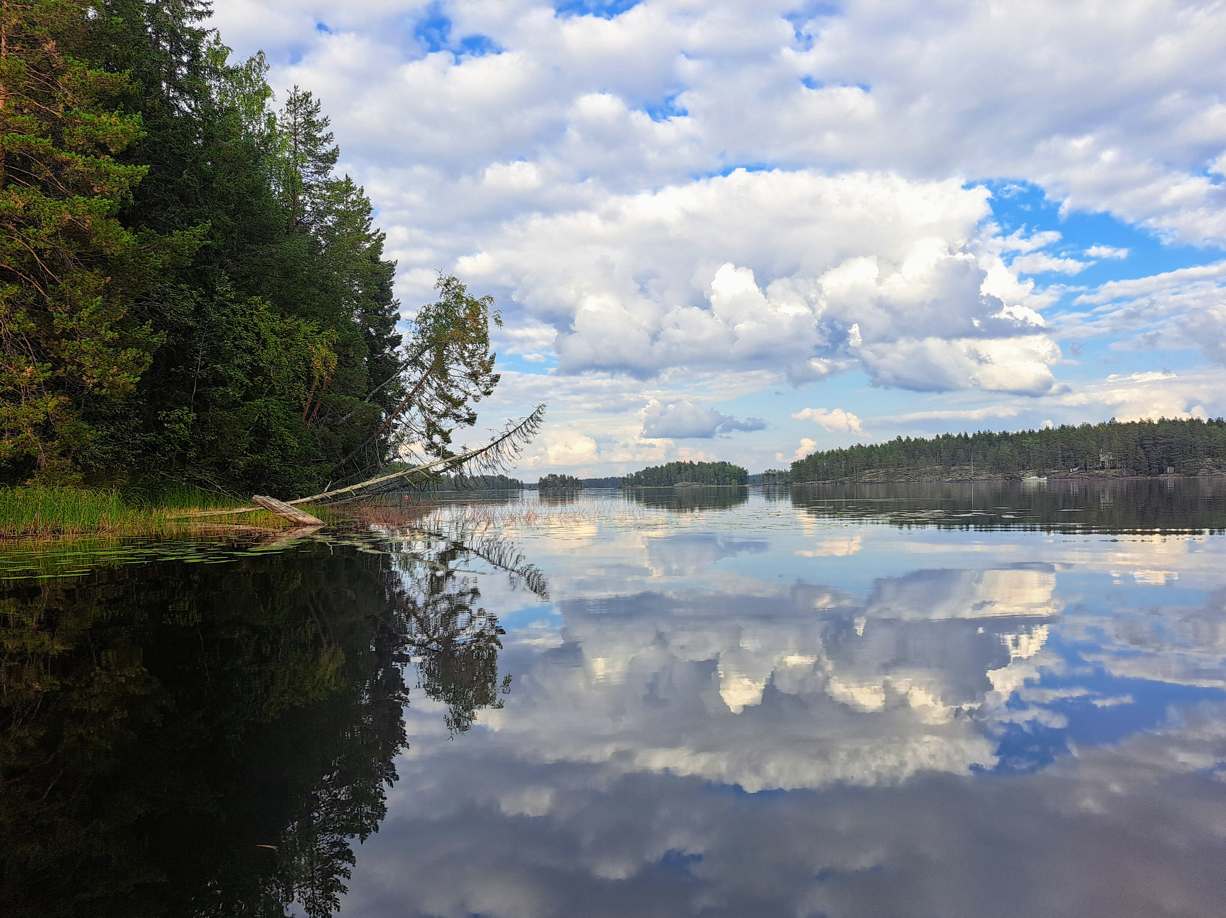Clouds reflect on the calm lake surface, rocky islands on the horizon.