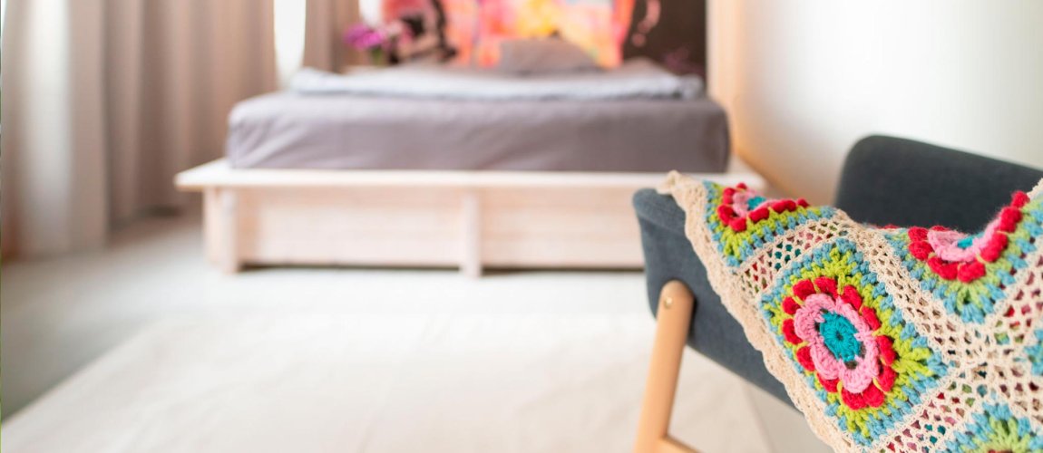 A chair with a blanket, a bed and colorful wallpaper softly blurred in the background.