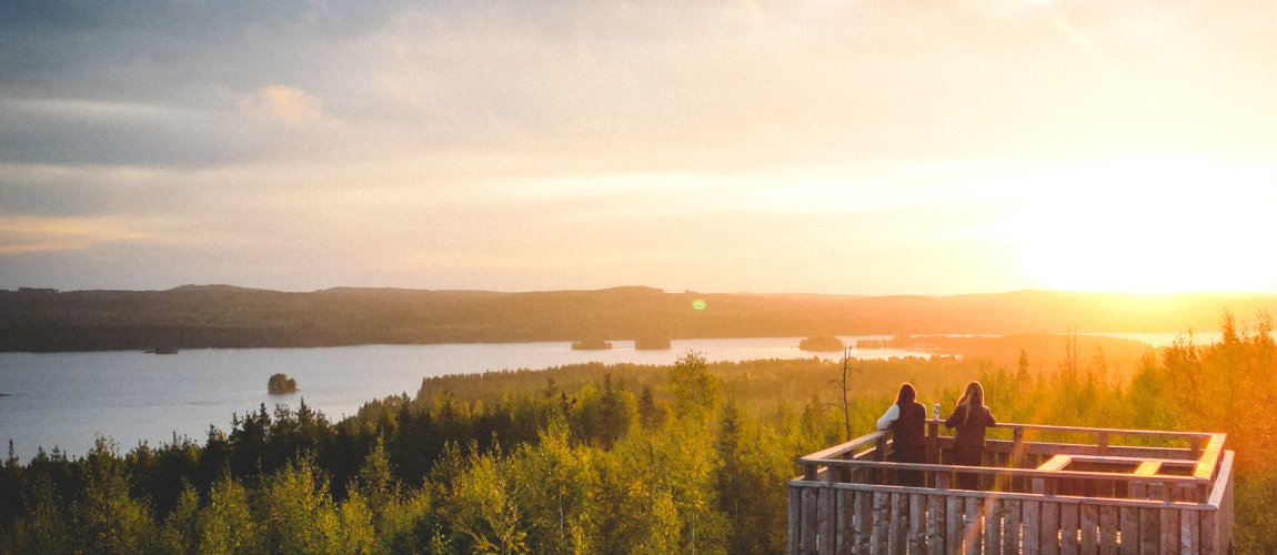 Two people are standing in the Äänemäki observation tower, looking at the landscape colored by the sunrise.